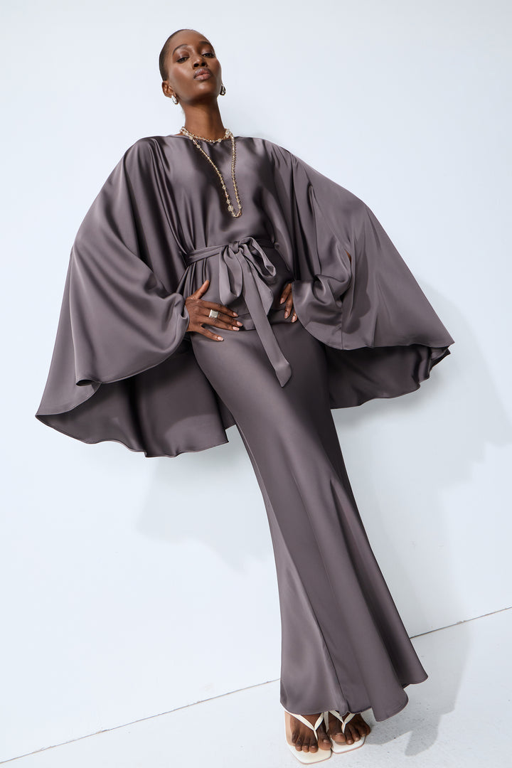 Modell im grauen Satin-Cape-Ärmel-Top und Rock Set bei Nacht - KYMA